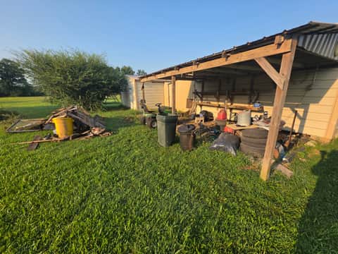 Backyard shed area cluttered with scrap wood, tires and trash cans before cleanup
